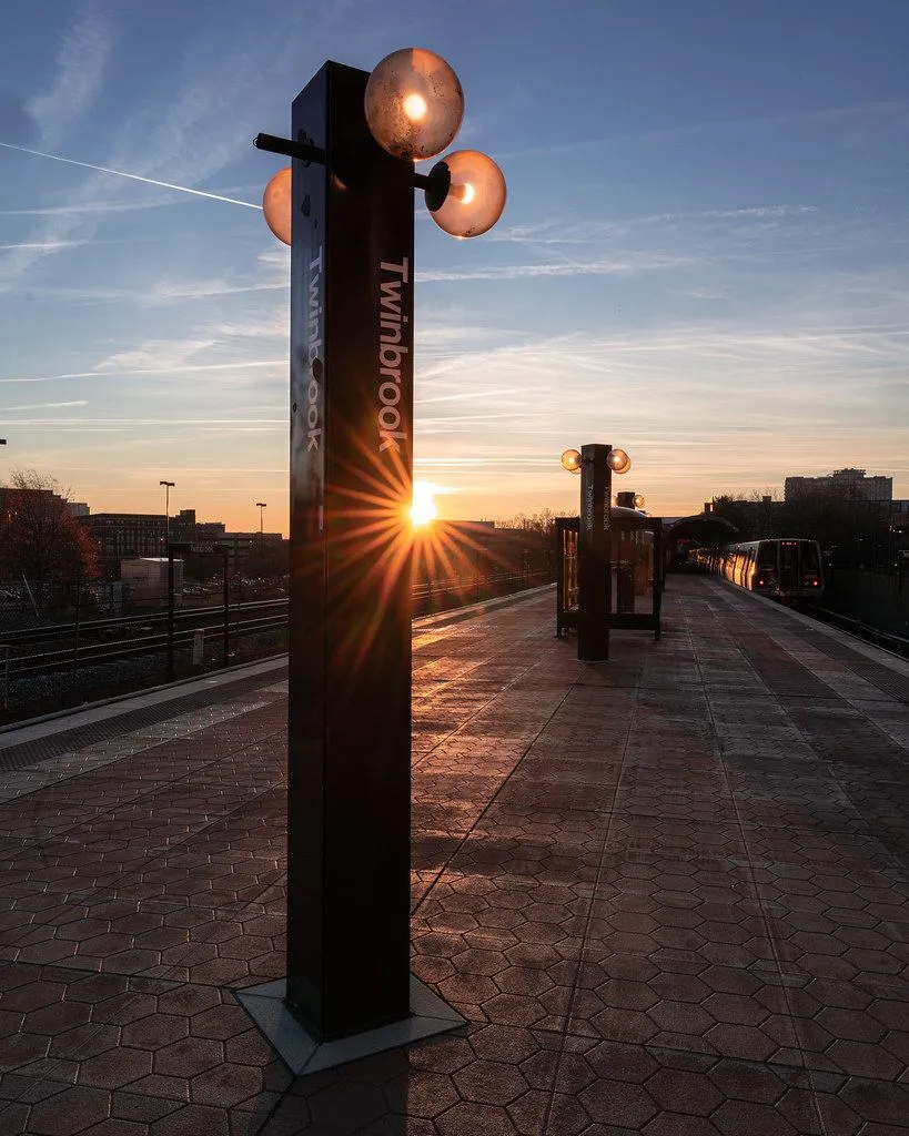 Un quai de gare désert éclairé par le soleil levant, avec un train qui approche au loin