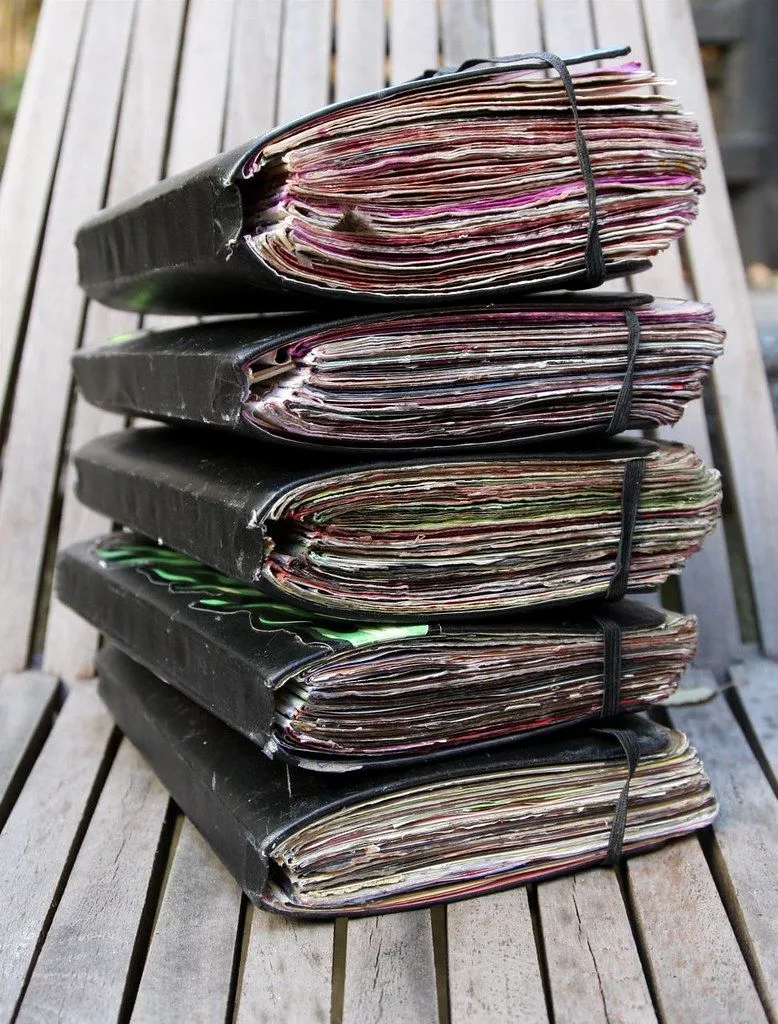 Une haute pile de carnets usés, tenus par des élastiques, sur un établi en bois