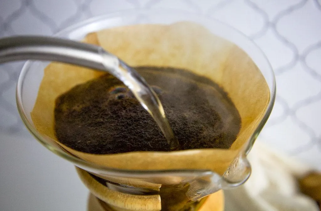 De l’eau versée sur du café moulu dans un filtre en papier conique, lors d’une préparation à la main