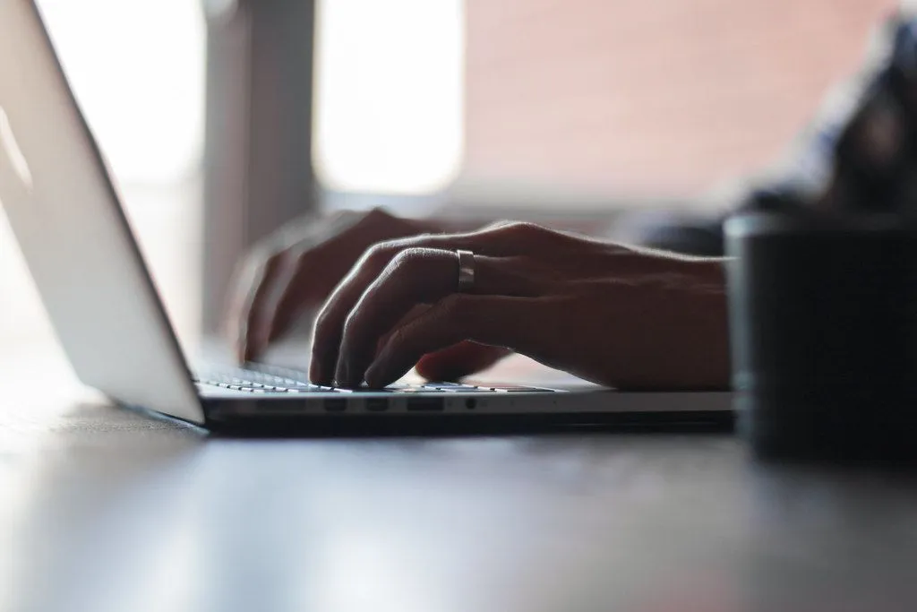 Gros plan sur deux mains qui tapent sur le clavier d’un ordinateur portable, l’une portant une alliance